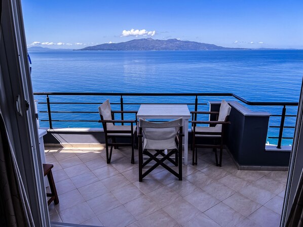 A balcony with a table and chairs overlooking a body of water and distant mountains.