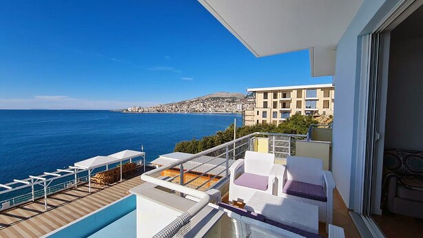 A balcony with a view of the sea and a distant town. - Planet Apartments (Sarandë)