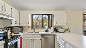 A modern kitchen with white cabinetry, stainless steel appliances, and a window providing a view of trees. - GolfView Chalet at the Woods Resort, Central Air and Heat (Hedgesville)
