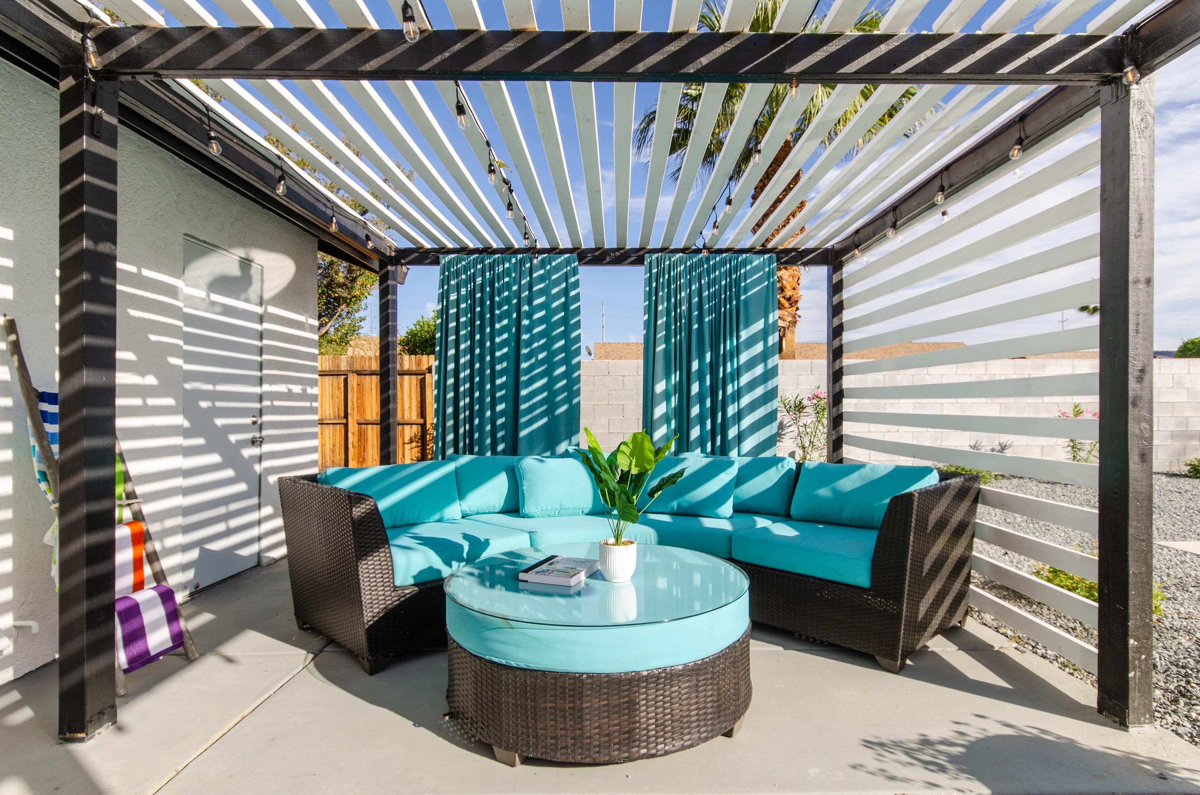 An outdoor seating area with a sofa and round table, under a pergola with striped fabric.
