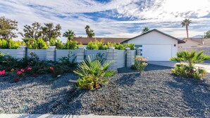 Un barrio residencial con una casa blanca, un muro de piedra y diversas plantas.