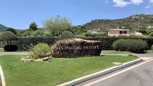 En stor sten med "is molas resort" indgraveret, omgivet af velholdt græs og hække, med en vej i forgrunden og bakker i baggrunden.