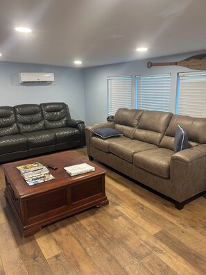 A living room with two leather sofas, a coffee table, and a wall-mounted air conditioner. - The Snapper House-Carrabelle (Carrabelle)