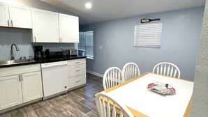 A compact kitchen with white cabinets and a dining area with a wooden table and white chairs. - The Snapper House-Carrabelle (Carrabelle)