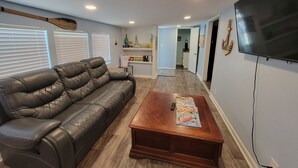 A living room with a leather sofa, a wooden coffee table, a flat-screen TV, and a kitchen area in the background. - The Snapper House-Carrabelle (Carrabelle)