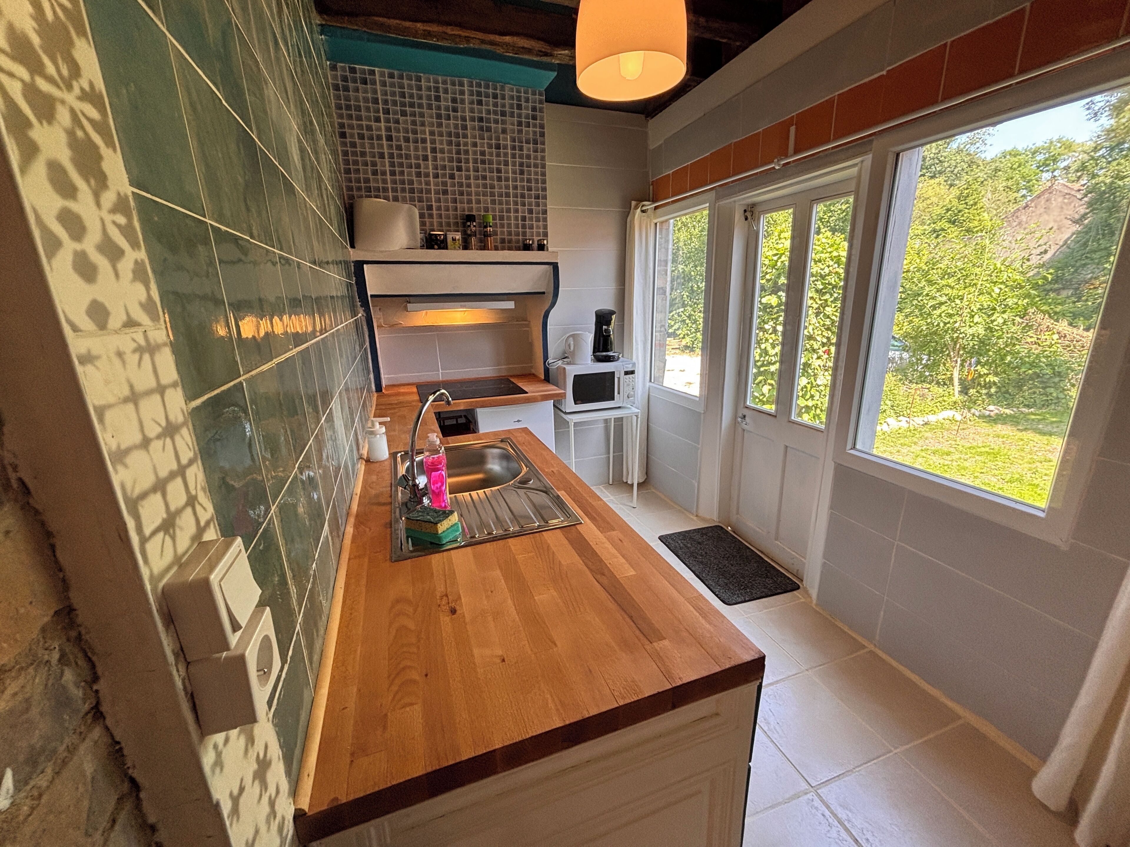 A modern kitchen with a wooden countertop, a sink, a microwave, and a window with a view of greenery.