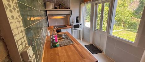 A modern kitchen with a wooden countertop, a sink, a microwave, and a window with a view of greenery.