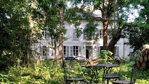 A garden with a table and chairs, surrounded by lush greenery and a large tree.