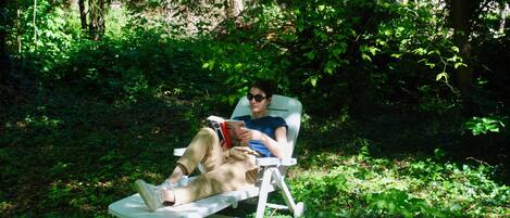 A person reclining on a white lounge chair in a lush, green outdoor setting.