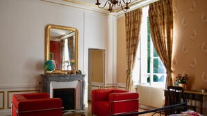 A room with a fireplace, red chairs, a bed with a colorful bedspread, a large mirror, and a window with curtains.