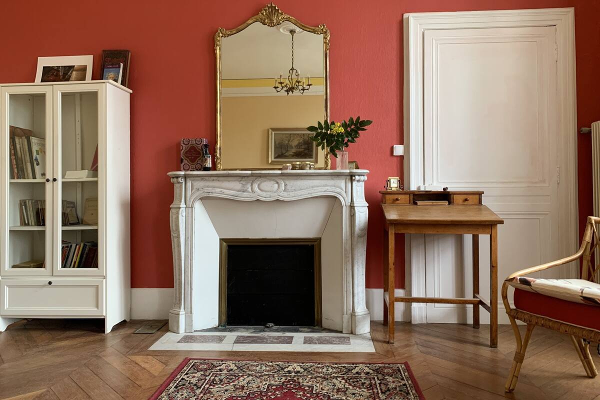 Una habitación con chimenea blanca, un espejo, una estantería y una silla de madera.