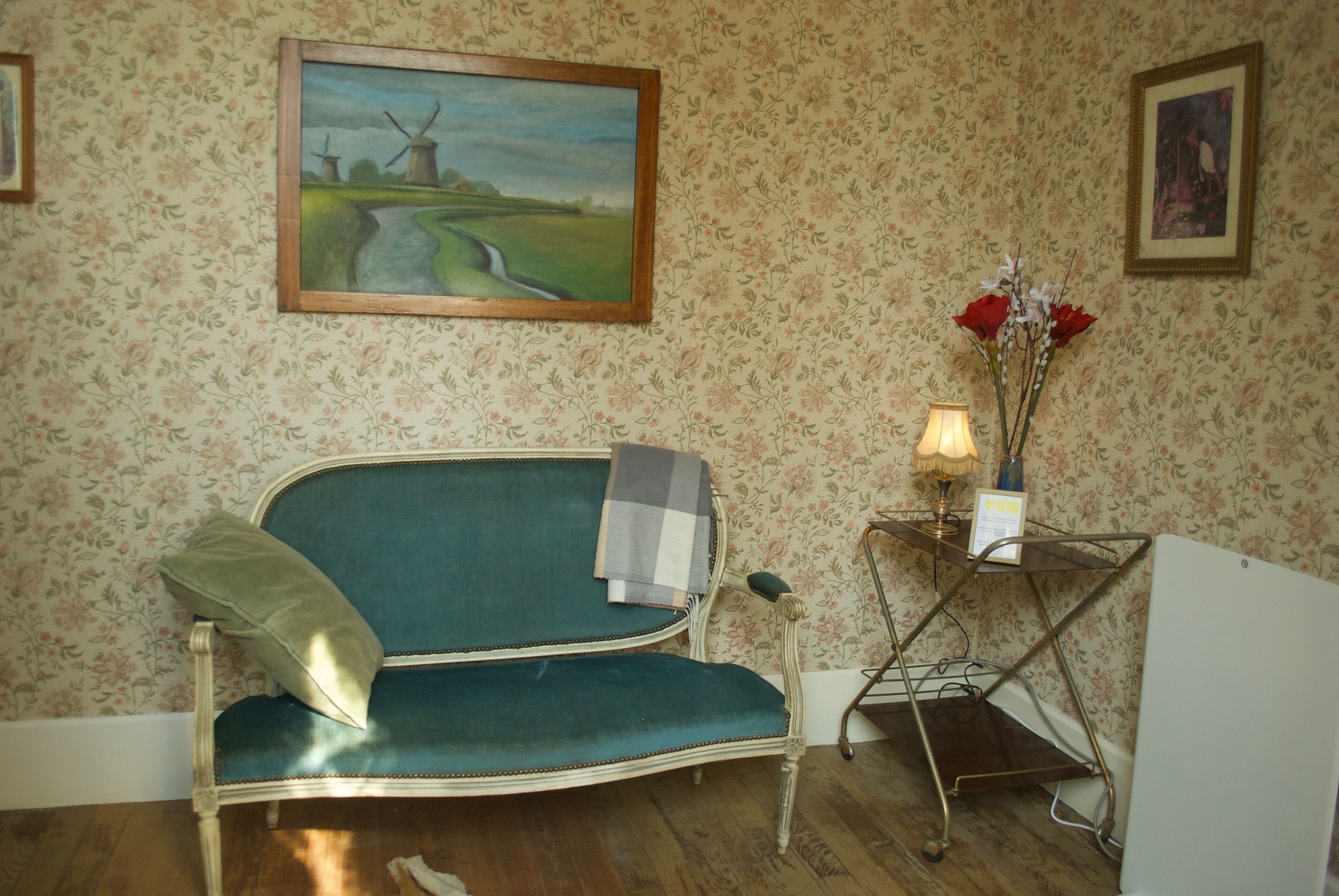 Une pièce avec un canapé de style vintage, une petite table avec une lampe et un papier peint à motifs floraux.