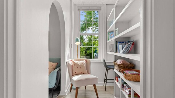A narrow hallway with a white chair, a bookshelf, and a window with a view of trees. - Physician`s Loft in the heart of downtown with 2 Free Parking Spots (Bar Harbor)