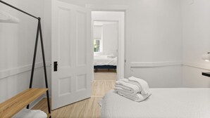 A bedroom with a bed, a wooden bench, a white door, and a view into another room. - Physician`s Loft in the heart of downtown with 2 Free Parking Spots (Bar Harbor)