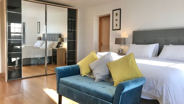 A bedroom with a large bed, a blue sofa with cushions, a wardrobe, and a mirror. - Marehay Hall Farm (Ripley)