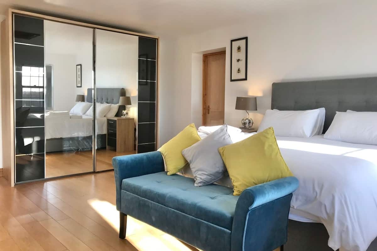 Ein Schlafzimmer mit einem großen Bett, einem blauen Sofa mit Kissen, einem Kleiderschrank und einem Spiegel.