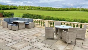 A patio with wicker furniture, a glass-top table, and a view of a green field. - Marehay Hall Farm (Ripley)