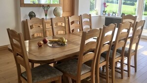 A dining area with a wooden table and chairs, a chandelier, a mirror, and a view of greenery outside. - Marehay Hall Farm (Ripley)