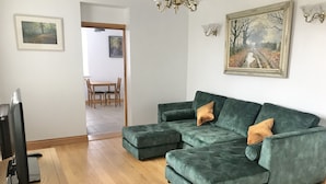 A living room with a sectional sofa, a television, and a dining area in the background. - Marehay Hall Farm (Ripley)