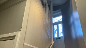 Eine Treppe mit einem Brandschutztürschild, ein Fenster mit Blick auf kahle Bäume und eine Tür mit weißem Rahmen.