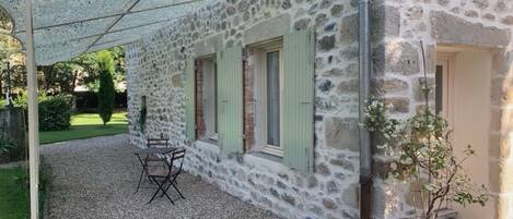 A stone building with a gravel patio, a table and chairs, and a potted plant.
