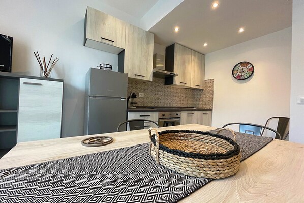 A modern kitchen with light wood cabinets, a stainless steel refrigerator, and a dining table with a woven basket.