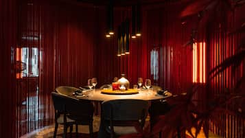 Une salle à manger à la lumière tamisée, avec une table ronde, des chaises et un luminaire central.