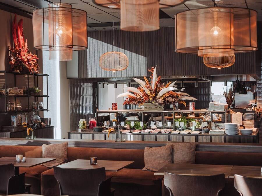 A modern restaurant interior with high ceilings, pendant lighting, and a central bar area.