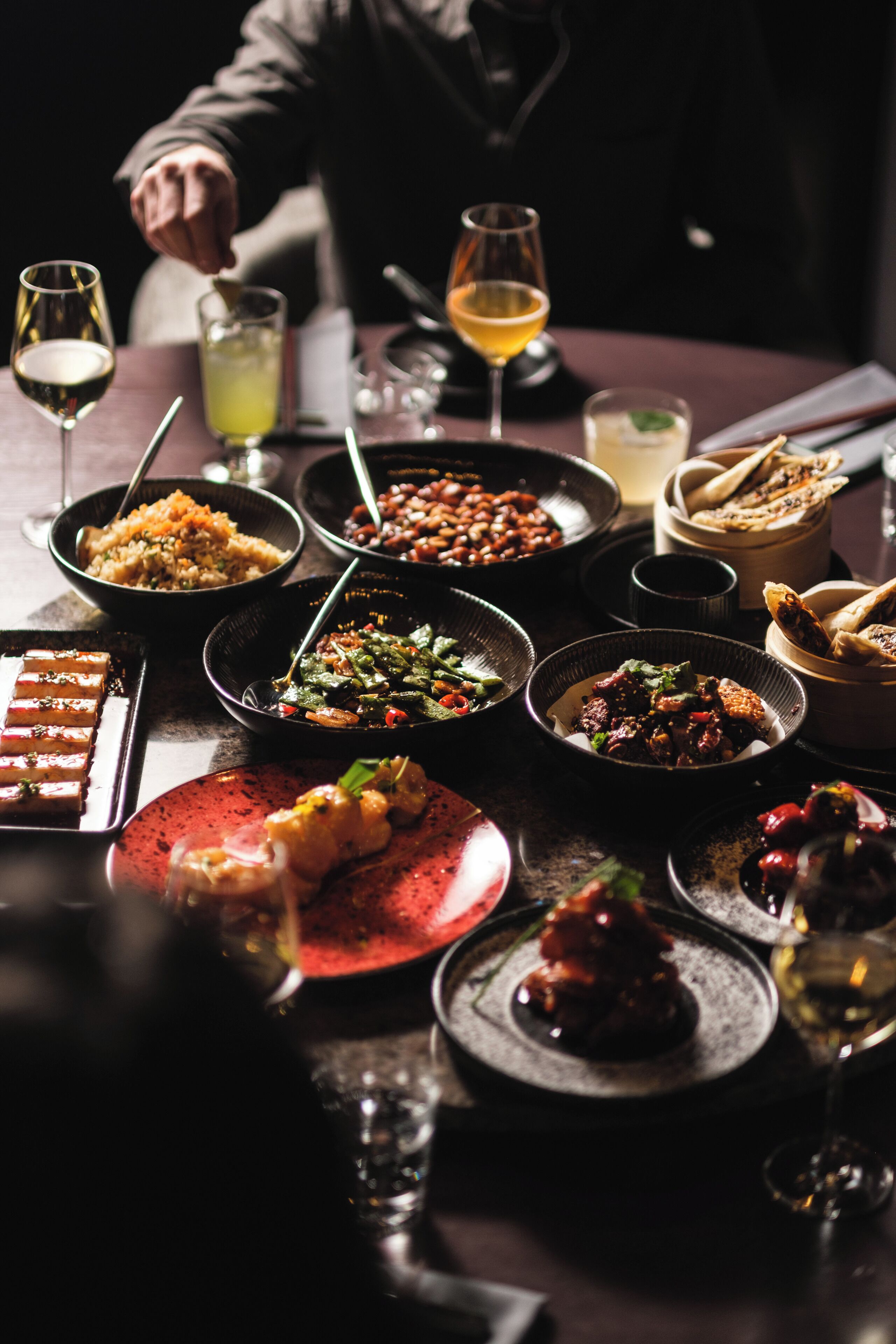 A table with various dishes and drinks, including a bowl of beans, a plate of meat, and a glass of wine.