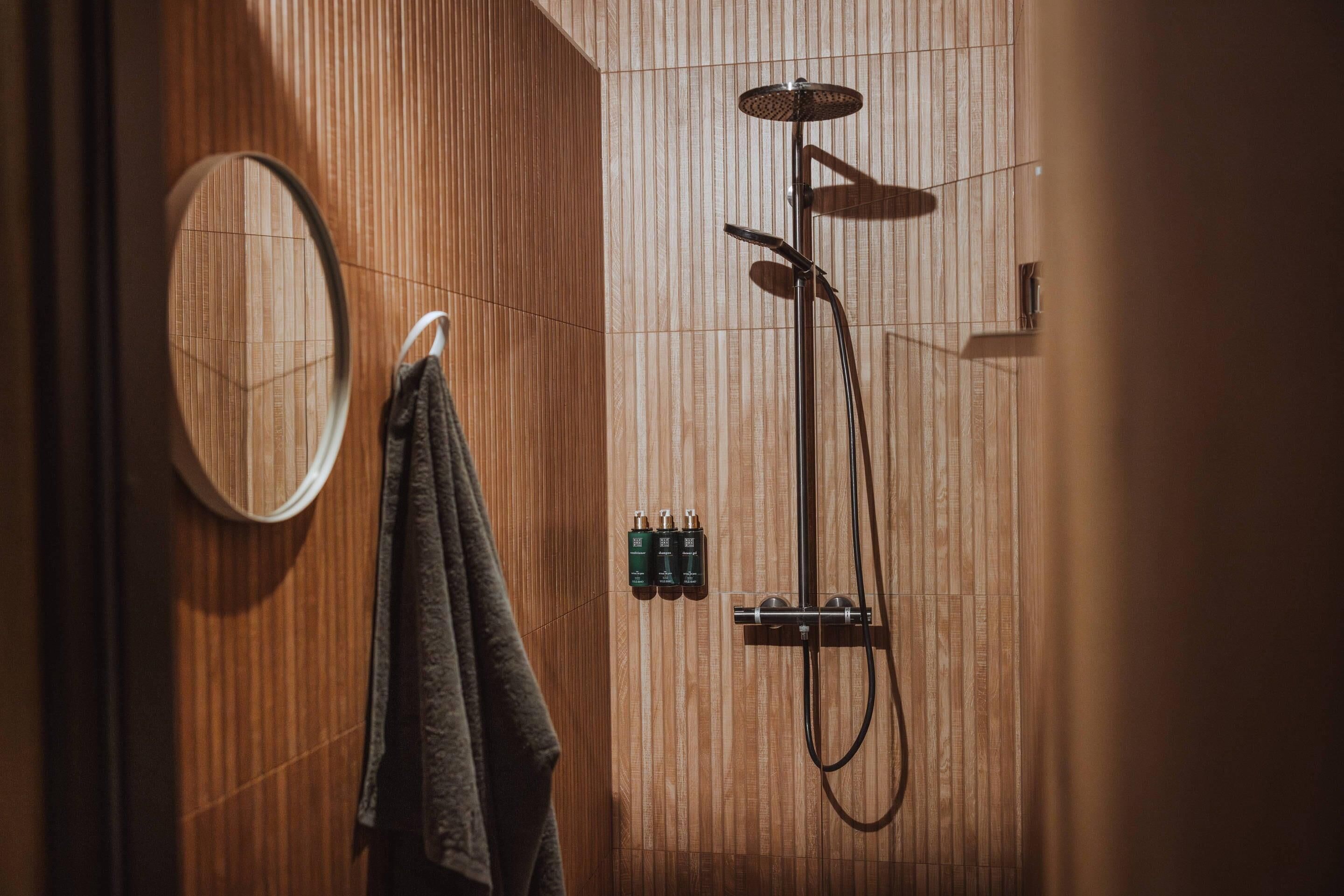 Pared de madera con un perchero, un espejo y un cabezal de ducha.