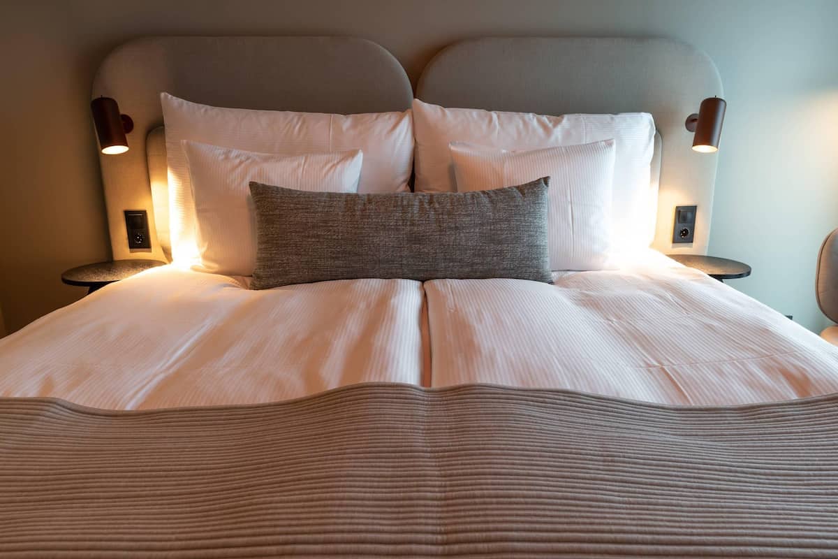 Ein ordentlich bezogenes Bett mit Kopfteil, zwei Nachttischlampen und einer Bedieneinheit an der Seite.