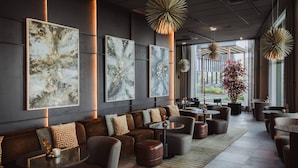 Un espace de détente moderne comprenant un canapé, des fauteuils et des tables, agrémenté d’œuvres d’art murales abstraites et d’un éclairage suspendu.