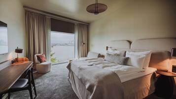 A hotel room with a large bed, a desk, a chair, a lamp, and a view of a body of water through the window.
