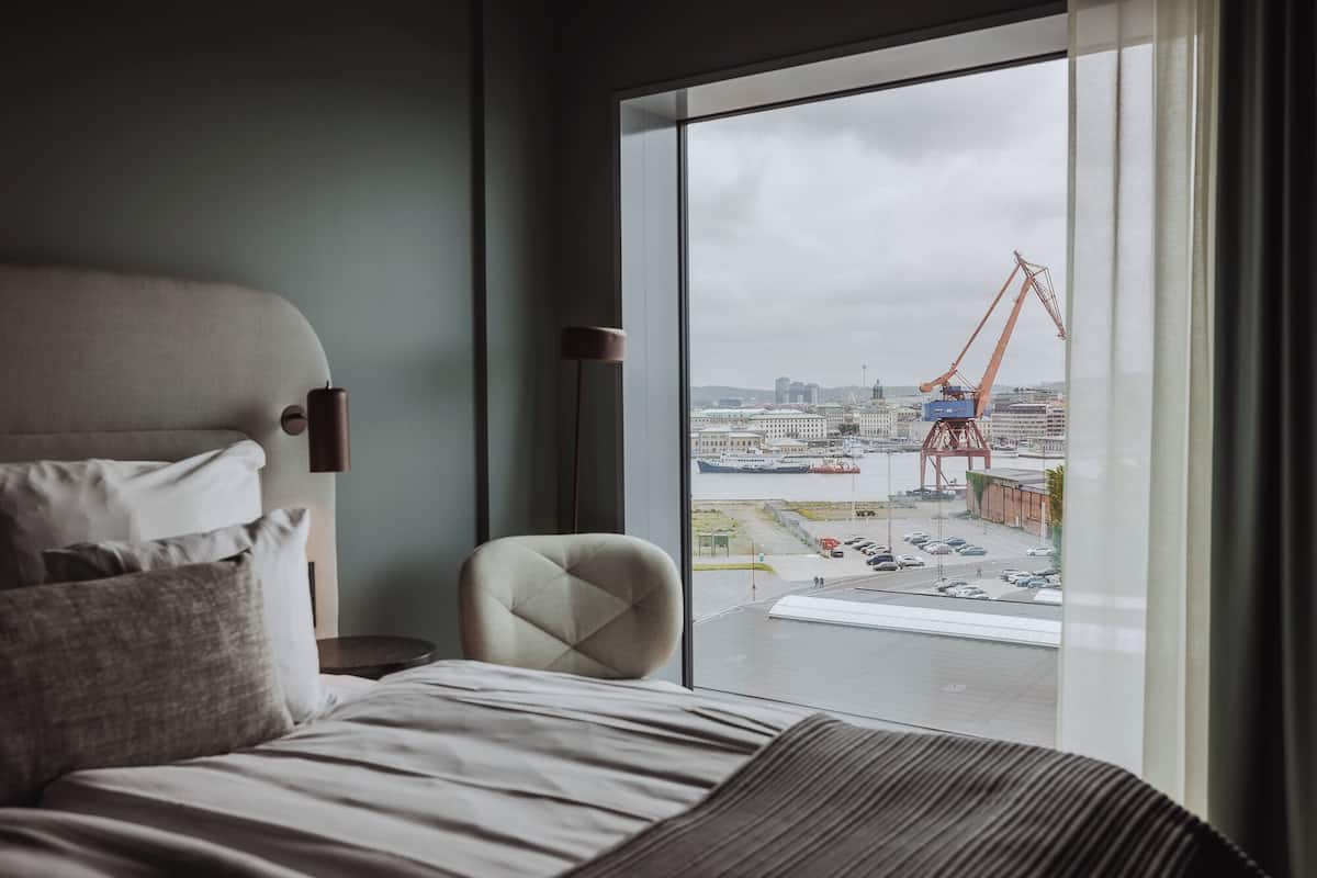 Ein Hotelzimmer mit großem Fenster, einem Bett, einem Sessel und einer Lampe.