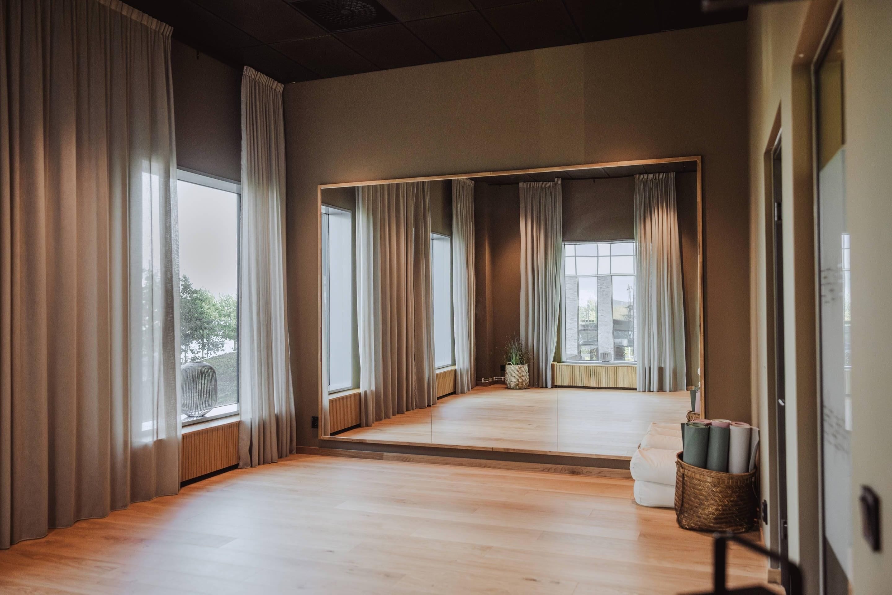 Una habitación amplia con ventanas grandes, un espejo y suelo de madera.
