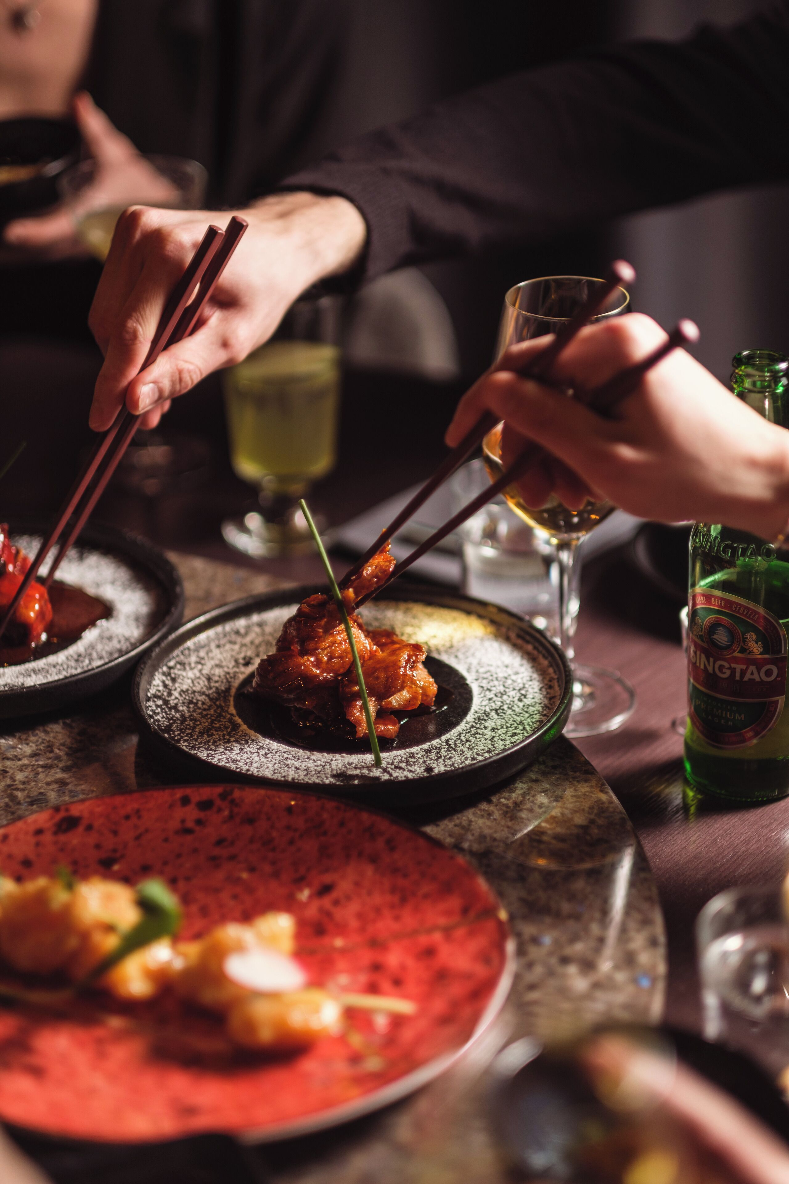 Una mesa de comedor con platos de comida, palillos y una botella de cerveza.