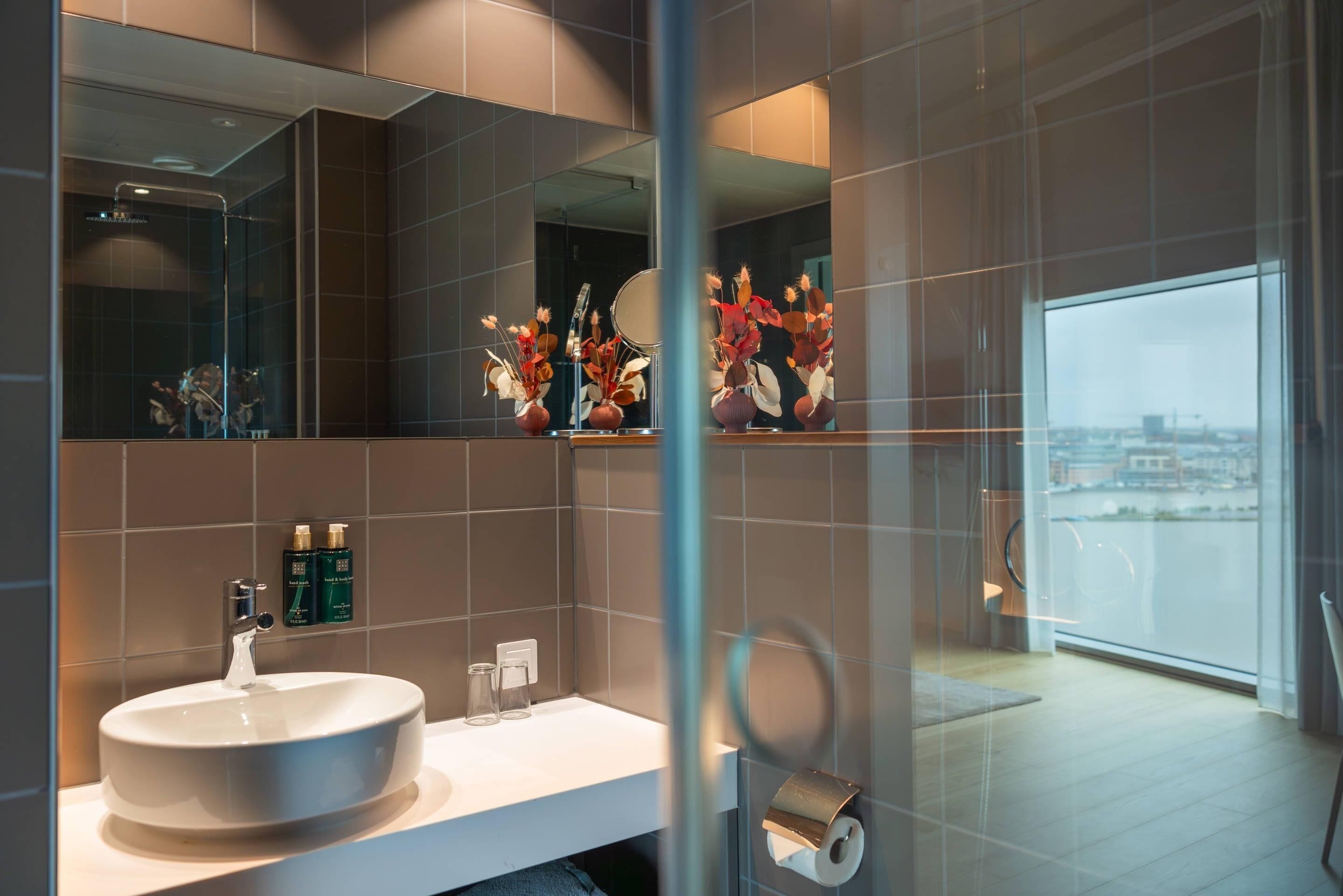 A modern bathroom with a large mirror, a round sink, and a toilet paper holder.