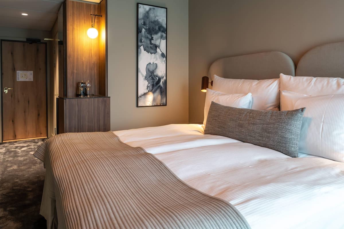 Ein Hotelzimmer mit Bett, Kissen, einem Wandbild, einem Holzschrank und einer Tür.