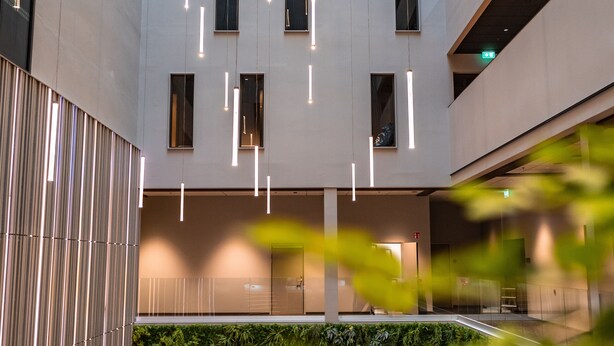 Un bâtiment moderne doté d’une cour intérieure aménagée avec un espace salon comprenant des canapés et une table basse, le tout entouré de luminaires verticaux et de verdure.