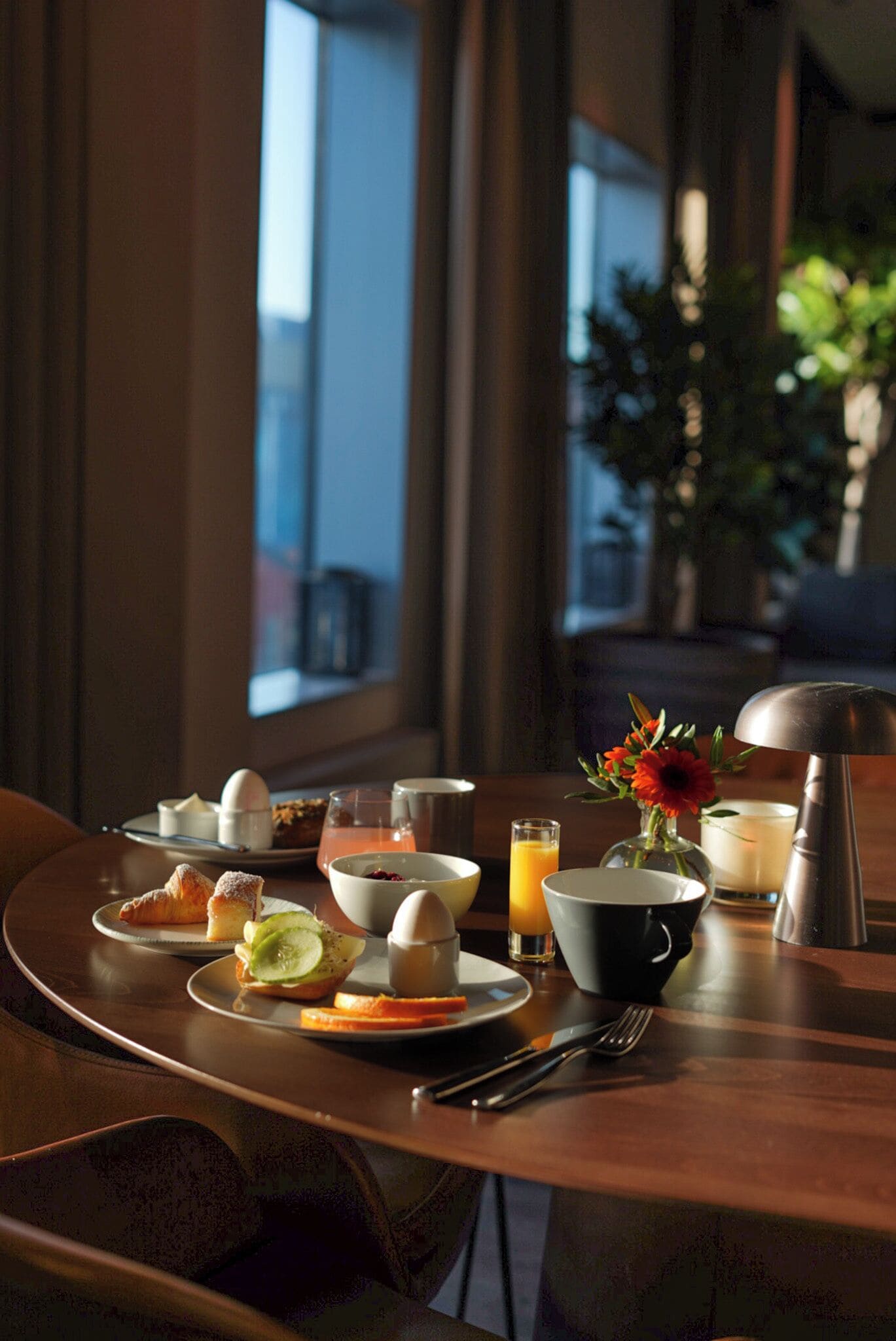 Desayuno con bollos, huevos y bebidas sobre una mesa con vistas al exterior.