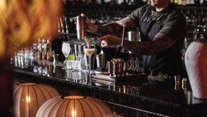 Un bar décoré de lanternes en papier suspendues, un barman préparant des cocktails et des étagères remplies de bouteilles.