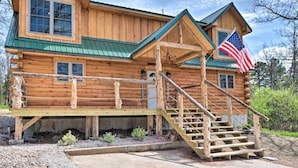 A wooden log cabin with a green roof, a porch, and a staircase leading to the entrance. - Newly built LOG Cabin-Float, Golf, Hike, Hunt, Fish, visit a winery...Relax! (cuba)