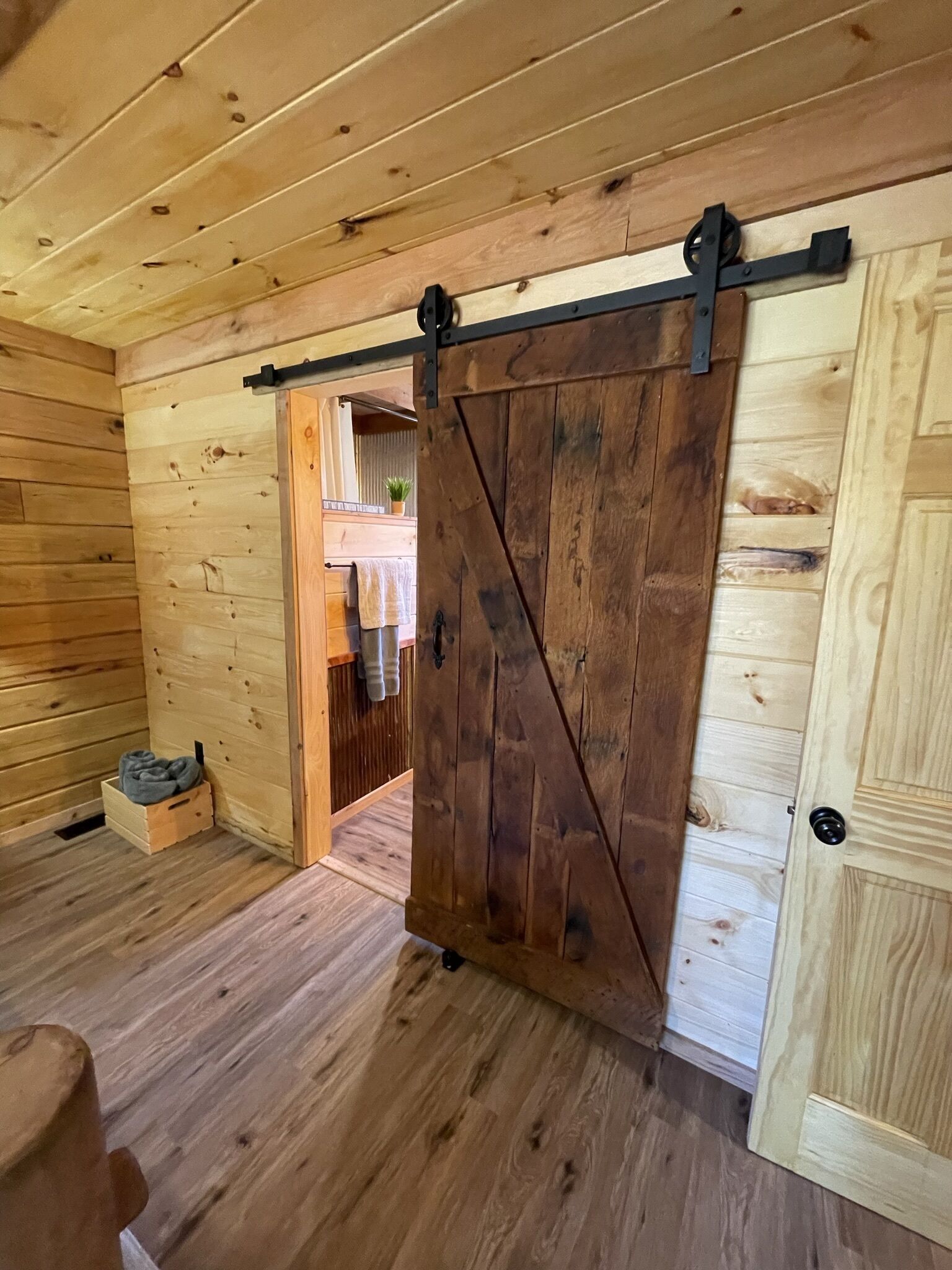 Interior de madera con una puerta corrediza de granero, una caja de madera pequeña y una toalla en el suelo.