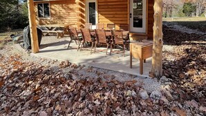 A wooden cabin with a covered patio area, featuring a dining table and chairs, and a large window. - Newly built LOG Cabin-Float, Golf, Hike, Hunt, Fish, visit a winery...Relax! (cuba)