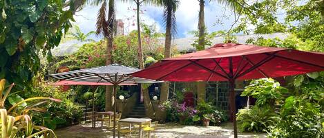 An outdoor patio area with stone flooring, yellow metal chairs, and red umbrellas providing shade.