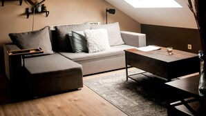 A cozy loft apartment with a sloped ceiling, a skylight, a sofa, a coffee table, and a small side table. - Cosy 2-bedroom Apartment in the Center of Hotton (Hotton)