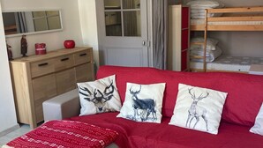 Un dormitorio moderno con un sofá rojo, un banco de madera, una mesita, un aparador y una cama litera.