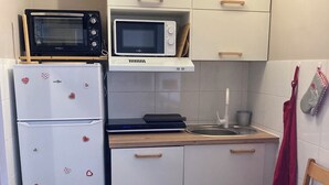 Una cocina compacta con gabinetes blancos, microondas, refrigerador y un lavamanos pequeño.