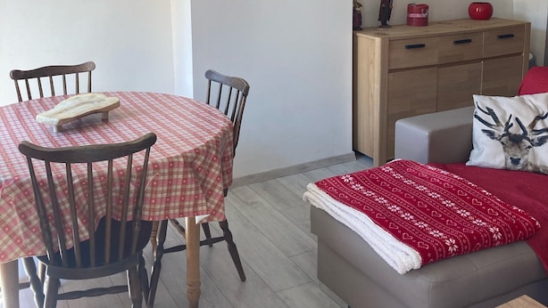 Un área de comedor con una mesa y sillas, un sofá y una cama con una manta roja.