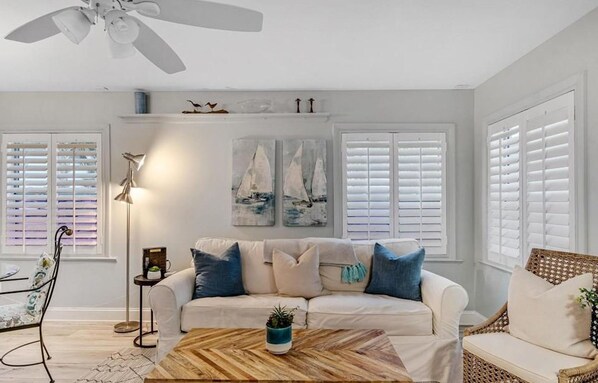 A living room with a white sofa, a wooden coffee table, and a ceiling fan.